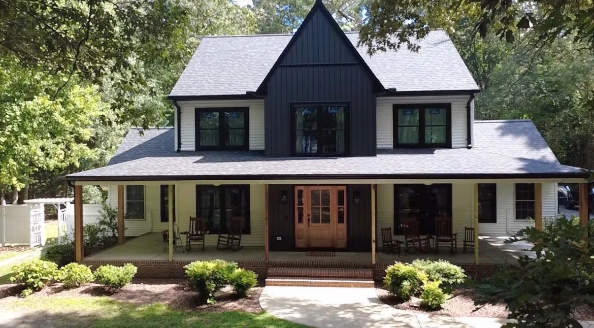 Black-and-white two-story home with a shingle roof and natural wood doors