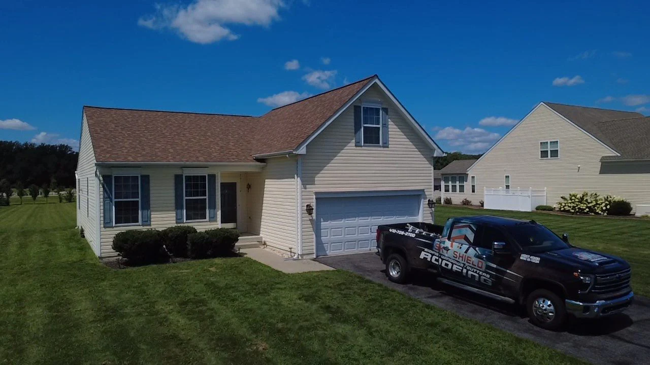Sky Shield Roofing truck beside a completed brown shingle roof on a light-colored home