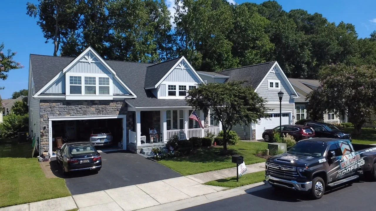 Sky Shield Roofing truck in front of a completed charcoal shingle roof on a gray craftsman-style home
