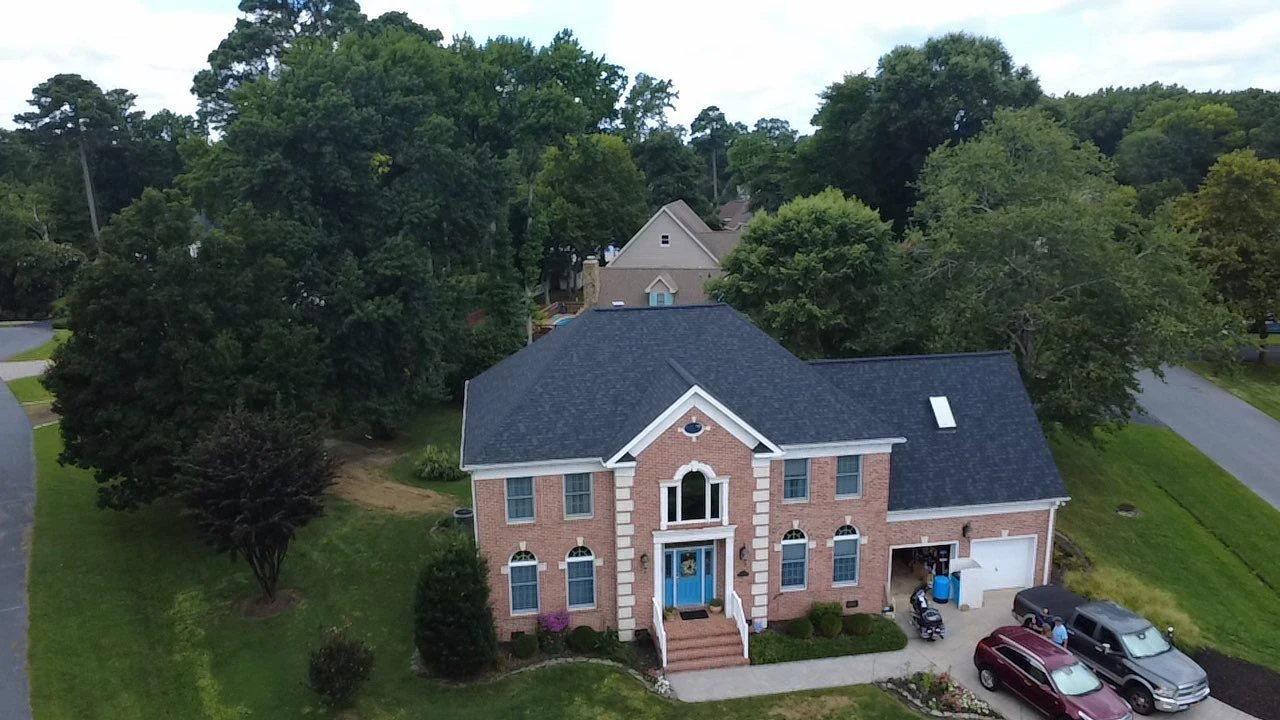Aerial view of a completed charcoal shingle roof on a two-story brick home
