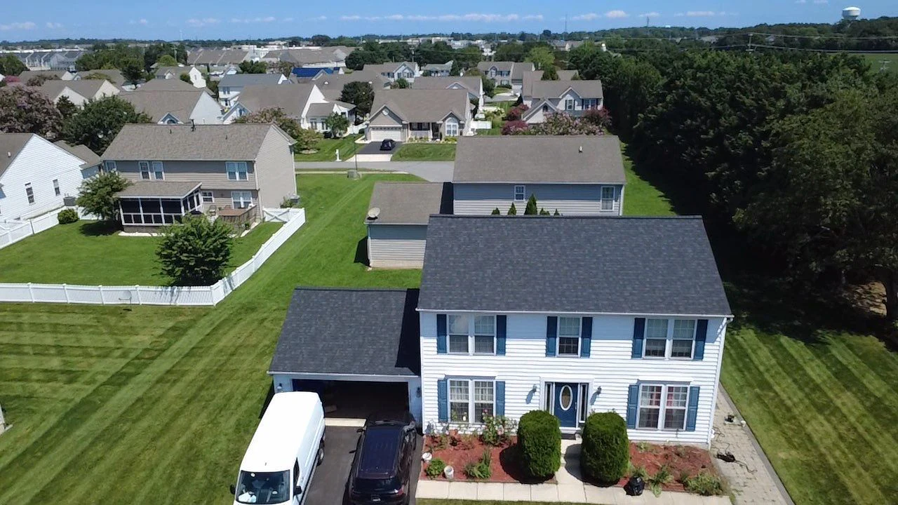 Aerial view of a completed charcoal shingle roof on a white colonial-style home