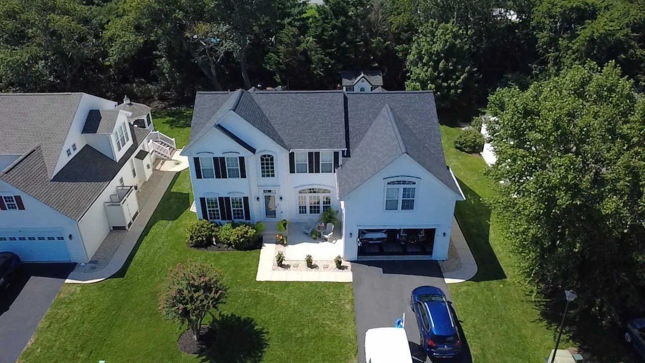 Aerial view of a completed charcoal shingle roof on a white two-story home
