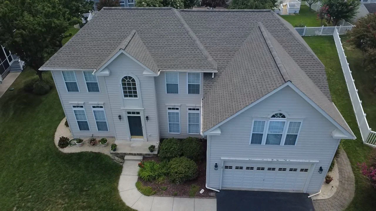 Aerial view of a completed tan shingle roof on a two-story home